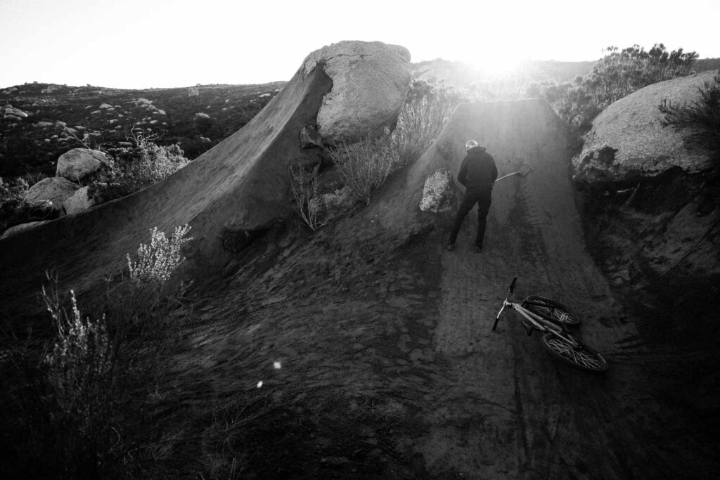 Black and white image of dirt biker shoveling ramp